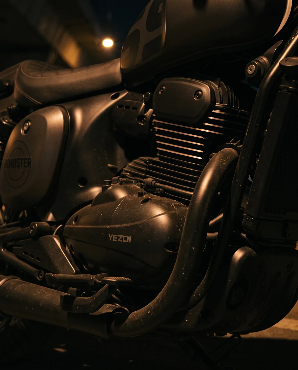 Close view of a Shadow Black Yezdi Roadster’s engine and exhaust header under sodium light.